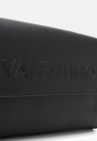 Borsa in pelle nera con logo "VALENTINO" in rilievo, che mostra una superficie texturizzata e un design pulito su uno sfondo bianco.