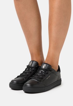 Baskets en cuir noir à profil bas, bout rond et fermeture à lacets. Elles présentent une semelle texturée et un logo discret sur le côté.