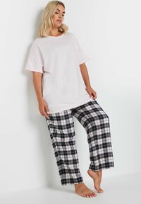 Jasnoróżowa, oversized koszulka z krótkim rękawem, zestawiona z czarnymi i białymi spodniami w kratę na piżamę, charakteryzująca się luźnym, wygodnym krojem.