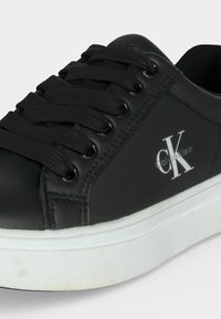 Μαύρο δερμάτινο παπούτσι Calvin Klein με μαύρα κορδόνια και λευκή χοντρή λαστιχένια σόλα, με το λογότυπο της μάρκας στην πλευρική επιφάνεια.