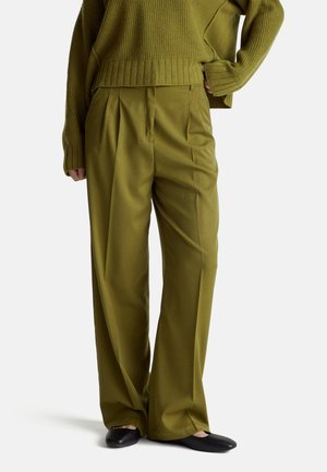 Pantalones de pierna ancha verde oliva con plisados, hechos de una tela suave. Combinados con un suéter de punto suelto a juego y unos zapatos planos negros.