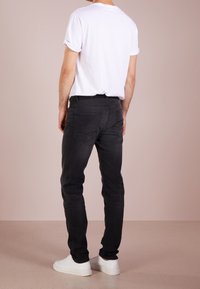 Svarta denimjeans med slim fit, bakfickor, som matchas med en vit t-shirt och vita sneakers, stående på ett ljust golv.