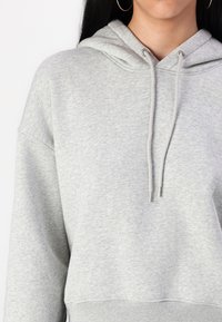 Sudadera gris en una suave mezcla de algodón. Presenta una capucha con cordón, un ajuste holgado y un dobladillo acanalado. Diseño minimalista sin patrones.