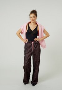 Czarny przezroczysty body, różowa oversize bluza z kapturem zarzucona na ramiona, brązowe spodnie o szerokich nogawkach w panterkę z różowym sznurkiem, gładka tkanina.