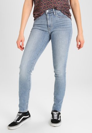 Jeans ajustados de algodón de color azul claro, con una cintura alta y un desvanecimiento sutil, combinados con zapatillas negras y blancas.