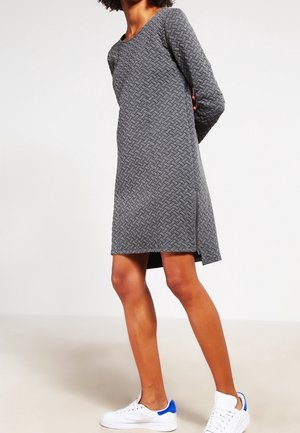 Abito grigio in tessuto intrecciato con scollo rotondo, maniche lunghe e spacchi laterali; indossato con sneaker bianche con accenti blu.