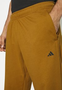 Bruine, zachte stoffen sweatpants met een elastische tailleband en zijzakken; heeft een zwart Adidas-logo op de onderste linkerbenen.