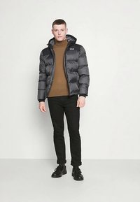 Czarna kurtka puchowa z kapturem, zapinana na zamek błyskawiczny z przeszyciami. Noszona na brązowym golfie i w połączeniu z czarnymi spodniami.