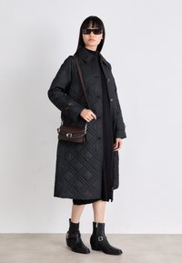 Μαύρο κουβερλί παλτό με μεγάλα κουμπιά, πλαϊνές τσέπες και γιακά. Συνδυάζεται με μαύρο τζ�έρσεϊ, καφέ τσάντα ώμου και μαύρες μποτίνες.