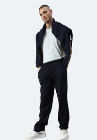 Dunkelblaue Baumwoll-Jogginghose mit elastischem Bund, kombiniert mit einem hellblauen T-Shirt und einem dunkelblauen Pullover, der über die Schultern gelegt ist.