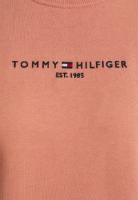 Sudadera de algodón en melocotón con cuello acanalado. Presenta el texto bordado en negro "TOMMY HILFIGER" y el logotipo, año de fundación 1985.