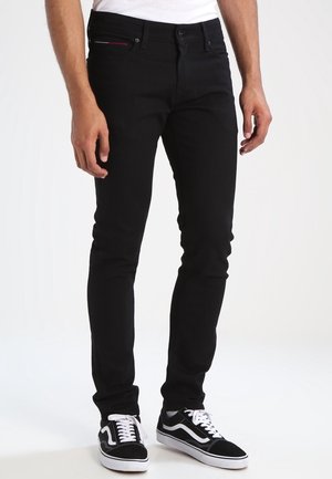 Mustat farkut slim fit -mallissa, joissa on viisi taskua ja huomaamaton punainen ommel etupuolella, yhdistettynä mustiin ja valkoisiin niin sanottuihin tennareihin.