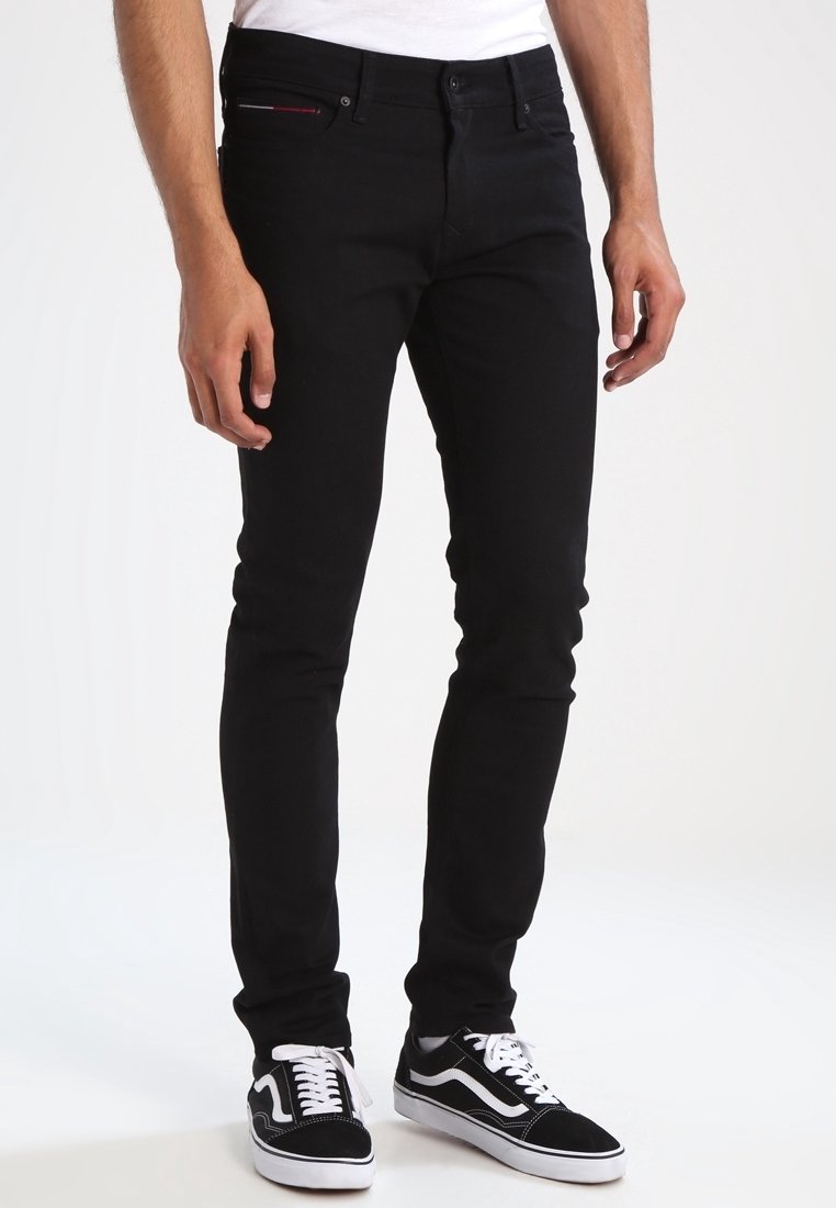 Black denim jeans with a slim fit, featuring five pockets and subtle red stitching detail at the front, paired with black and white sneakers.