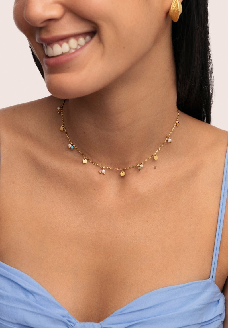 El collar en tono dorado presenta pequeños encantos coloridos y medallones circulares, exhibiendo un diseño delicado con texturas y acentos variados.