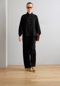 Sorte stripete skjorte med knapper, svarte bukser og lysebrune slip-on sko. Tilbehør inkluderer oransje solbriller og en brun clutch.