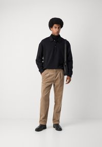 Camisa polo negra con collar, pantalones de pana beige y botas gruesas negras. Diseño minimalista con un bolso de hombro.