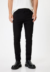 Musta farkut slim fit -mallilla, joissa on viisi taskua, napin suljenta ja etupistolet, yhdistetty mustiin nilkkabootseihin.