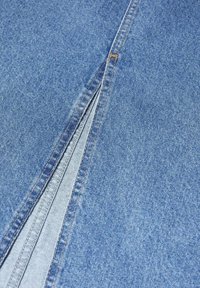 Tissu en denim bleu avec une ouverture de fermeture éclair visible. Le matériau est texturé et lisse, avec des coutures contrastées le long des bords.