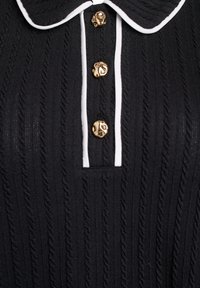 Czarny sweter z dzianiny ozdobiony fakturowanym wzorem warkocza, białą lamówką na kołnierzu oraz trzema złotymi guzikami z tłoczonymi wzorami.