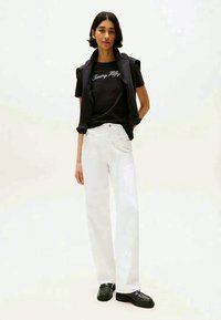 T-shirt noire avec le texte "Tommy Hilfiger", pantalon large blanc, chaussures noires, gilet noir en couches ; textures lisses, design minimaliste.