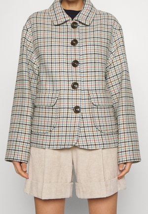 Femme portant une veste boutonnée à carreaux multicolores avec de gros boutons foncés et un short en velours côtelé beige avec ourlet retroussé.