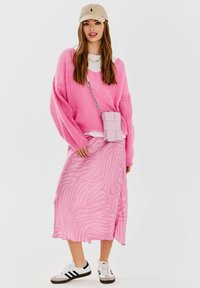 Różowy, oversize'owy sweter, maxi spódnica w różowy wzór zebry, jasnoróżowa torebka na ramię oraz białe sneakersy z czarnymi akcentami.