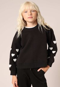 Zwarte sweatshirt met witte hartpatronen op de mouwen, ribgebreide manchetten en zoom, met een ronde hals en een losse pasvorm. Zachte stoftextuur.