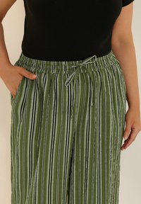 Gröna randiga byxor med elastisk midja och justerbar snörning. Har vertikala ränder i olika bredder, med tunna svarta accenter.