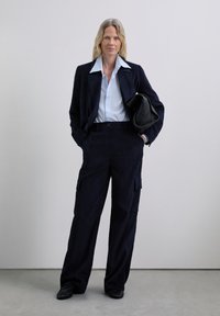 Navy corduroy blazer and matching cargo pants, paired with a light blue shirt. Black handbag. Flat shoes. Simple design, relaxed fit.