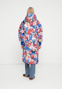 Cappotto lungo imbottito floreale in vivaci motivi rossi, blu e bianchi. Presenta un cappuccio a collo alto e polsini elasticizzati, con una vestibilità ampia e tasche laterali.