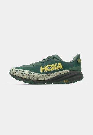 Green running shoes with a textured upper, featuring a yellow brand logo, a patterned light-colored sole, and a Vibram logo on the outsole.