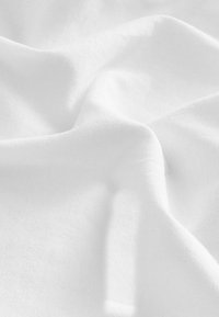 Tessuto bianco con una superficie morbida e testurizzata, che mostra lievi pieghe e increspature, riflettendo leggermente la luce.