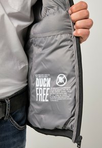 Graue Pufferjacke mit synthetischer Füllung, ausgestattet mit einem "DUCK FREE"-Schild in weißem Text und einem Entensymbol ohne Enten. Mit Reißverschlussöffnung.