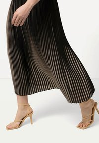 Abito plissettato con righe nere e beige, tessuto fluido e taglio svasato. Abbinato a sandali con tacco alto e cinturini color nude.