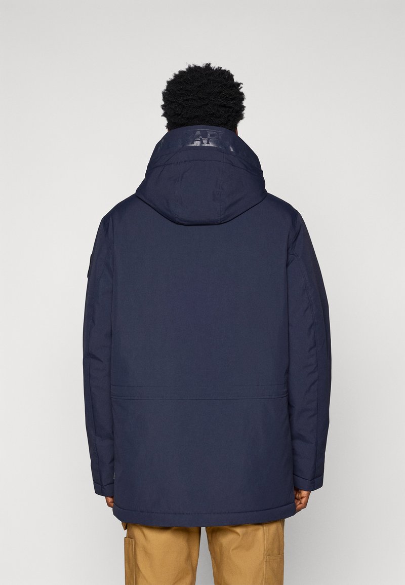 Parka bleu marine avec capuche, présentant un col texturé et des détails de logo cousus. Le matériau semble lisse et la coupe est ample.