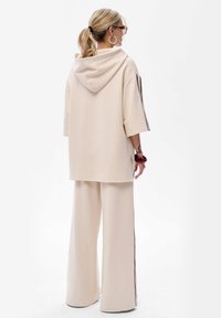 Beżowy, oversize'owy hoodie z kapturem z tyłu i krótkimi rękawami, w połączeniu z szerokimi beżowymi spodniami z bocznymi paskami. Gładka tekstura materiału.