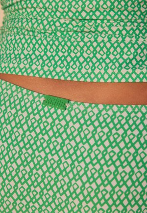Grön mönstrad tyg med diamantformade mönster på en ljus bakgrund, med en kontrasterande brun midjeband och en grön etikett märkt "SCION."