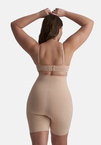 Body de control color beige con tirantes ajustables y diseño sin costuras, que llega hasta la mitad del muslo, con un cierre de gancho y ojo en la parte posterior.