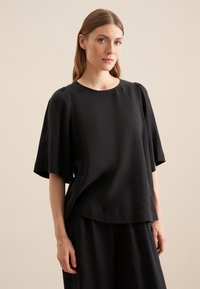 Top in lino nero con maniche corte e larghe, scollo rotondo e vestibilità rilassata. Caratterizzato da una consistenza morbida e design minimalista.