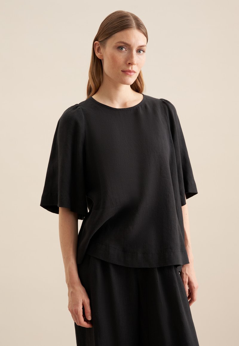 Top in lino nero con maniche corte e larghe, scollo rotondo e vestibilità rilassata. Caratterizzato da una consistenza morbida e design minimalista.