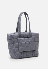 Sac fourre-tout matelassé gris avec deux poignées, présentant une surface texturée avec un motif en grille et une poche à rabat à l'avant.
