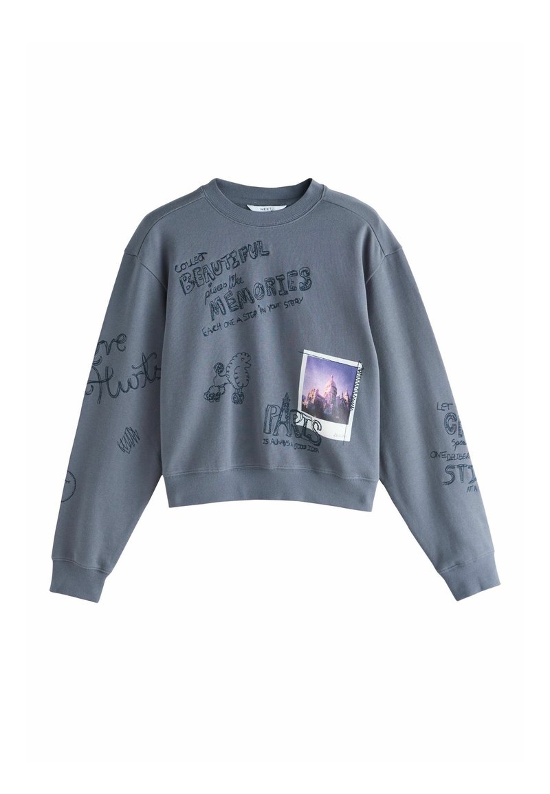 Sweat-shirt gris avec texte manuscrit, dessin au trait d’un caniche et impression photo d’un bâtiment éclairé au crépuscule.