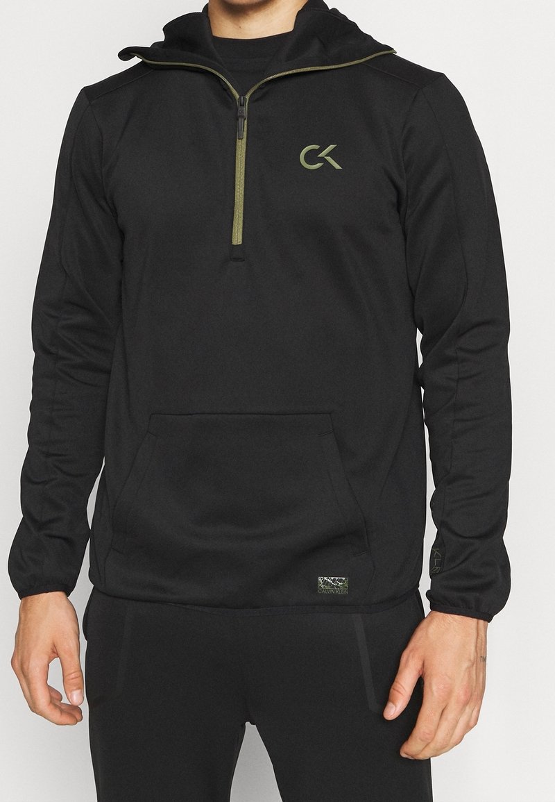 Felpa nera a zip con cappuccio, caratterizzata da un logo verde e dettagli con zip. Realizzata in un tessuto leggero e liscio con una tasca frontale.