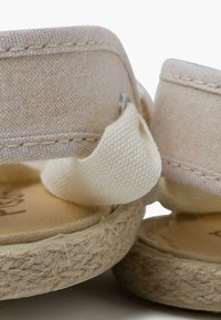 Sandalias de tela beige con suelas de esparto, que cuentan con una suave correa de algodón y un detalle decorativo de metal cerca del tobillo.