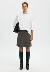 Bijela oversize majica, siva raširena vunena suknja, crne kožne čizme do koljena i crna torba s kružnom ručkom.