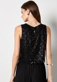 Top negro sin mangas con un diseño de lentejuelas en forma de concha, que presenta un detalle de espalda con abertura en forma de llave y un dobladillo inferior de textura suave.