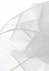 Weißes Netz-Fascinator mit geschichteten Rüschen und einer geschwungenen Silhouette, befestigt an einem dünnen, flexiblen Haarband für sicheren Sitz.