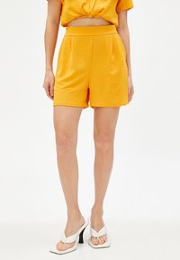 Geel short met een gestructureerde afwerking, elastische tailleband, zijzakken, gecombineerd met witte hoge sandalen. Eenvoudig, schoon ontwerp.