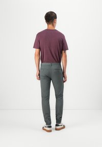 Férfi öltözet, amelyben egy rövid ujjú bordó póló és slim-fit szürke nadrág szerepel. A nadrág hátul zsebekkel rendelkezik és sima textúrájú, sportcipővel párosítva.