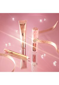 Drei Schönheitsprodukte auf einer reflektierenden rosa Oberfläche: ein goldener Highlighter in einer Tube, ein rosa Lippenstift mit einem gesteppten Design und ein rosa Lippenstiftstift.